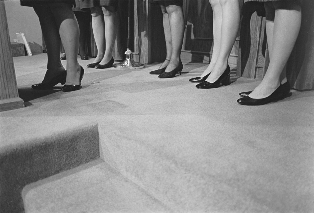Women's legs and feet in dress shoes on carpeted floor.