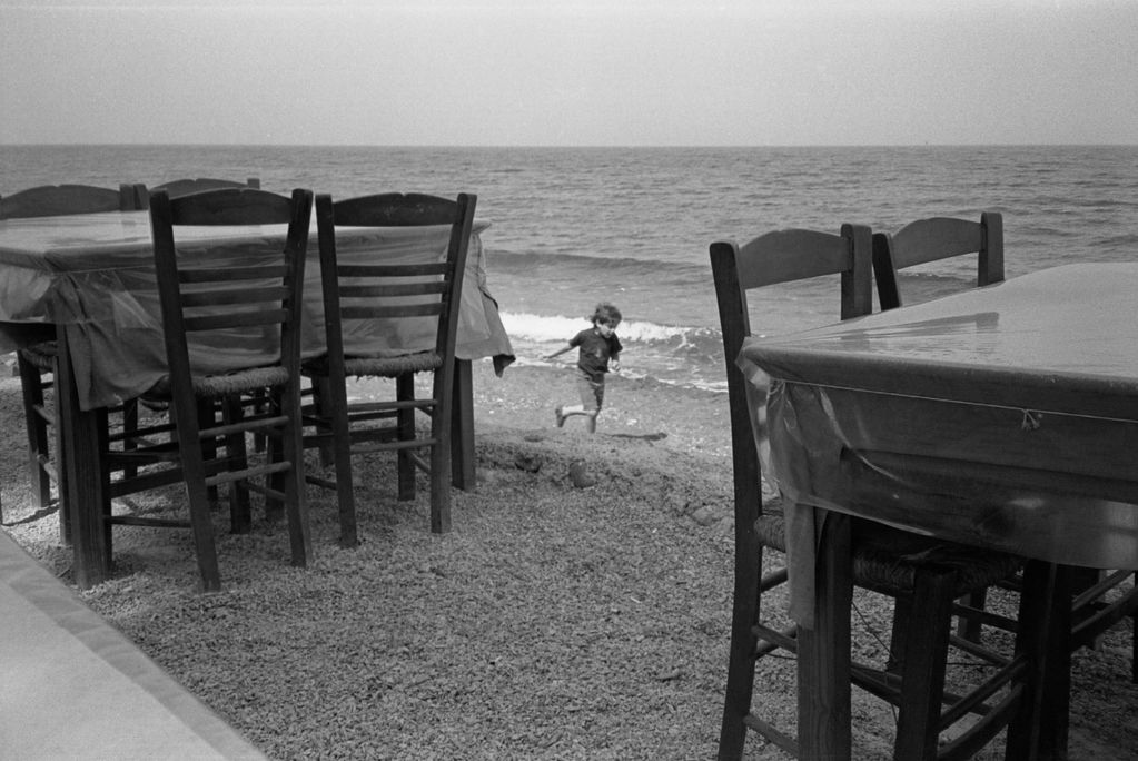 Child playing near beach-side tables.