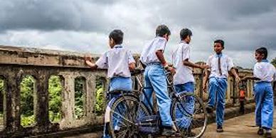 Schoolboys in uniforms with a bicycle on a cloudy day.