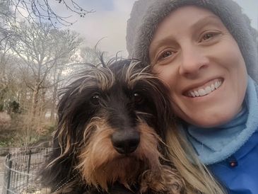 Woman in winter hat smiling with her dog outdoors.