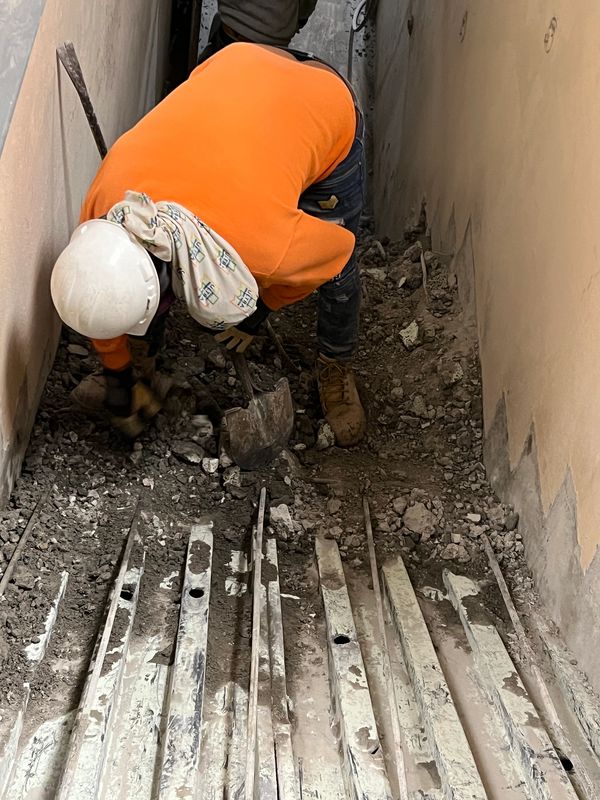 Construction worker in an orange jacket digging in a narrow space.