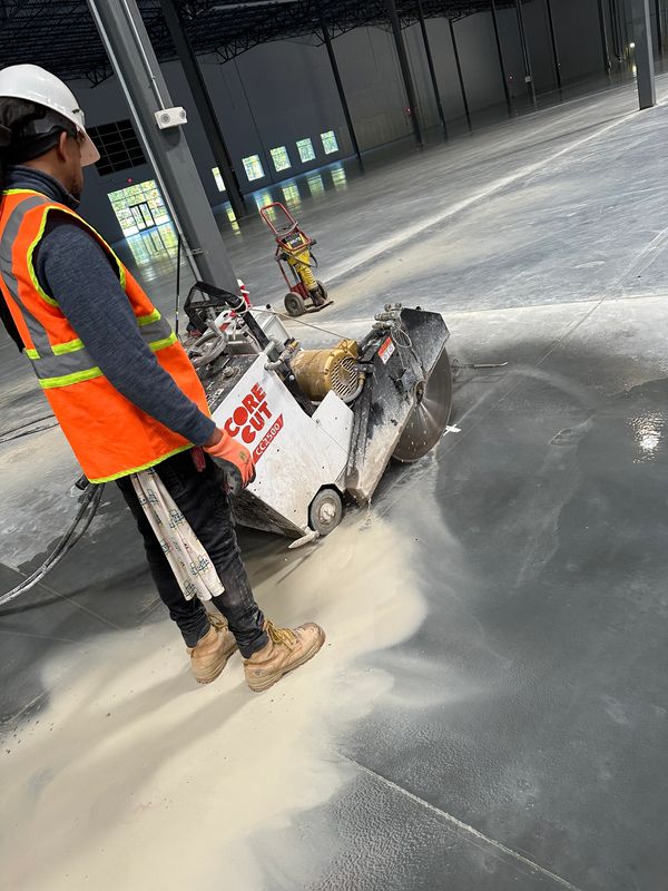 Worker using a concrete cutting machine inside a large industrial building.