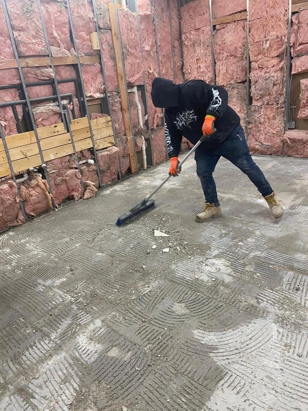 Worker sweeping debris in an unfinished room with exposed insulation.