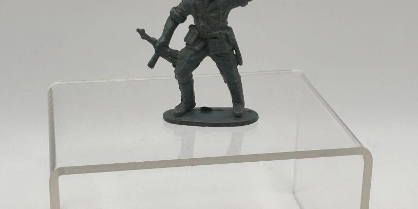 A green plastic toy soldier holding a rifle, standing on a clear acrylic block.