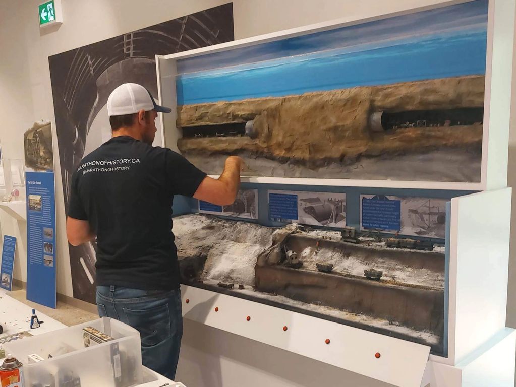 A man interacts with a detailed historical tunnel model in a museum exhibit.