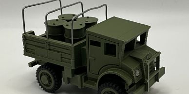 Green military-style toy truck carrying barrels on its flatbed.