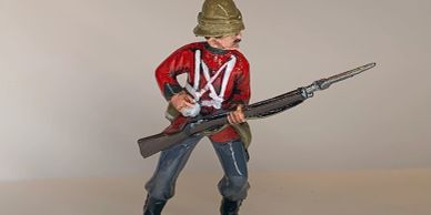 A painted toy soldier holding a rifle with a bayonet, dressed in a red jacket and pith helmet.