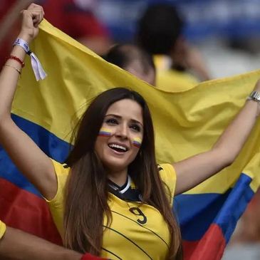 Woman proudly waving Colombian flag with face paint at a sports event.