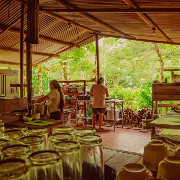 Two people working in a rustic open-air kitchen surrounded by greenery.