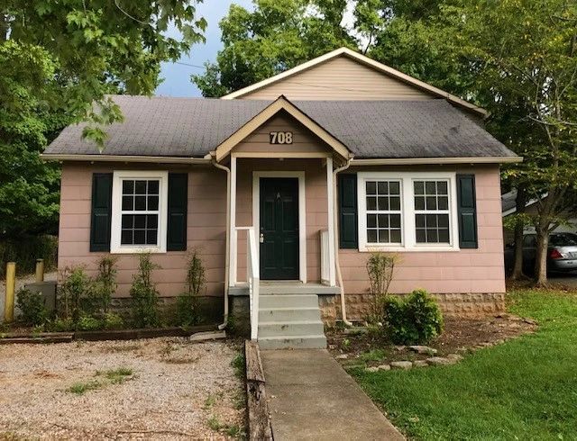 Small pink house with green door and white windows surrounded by trees.