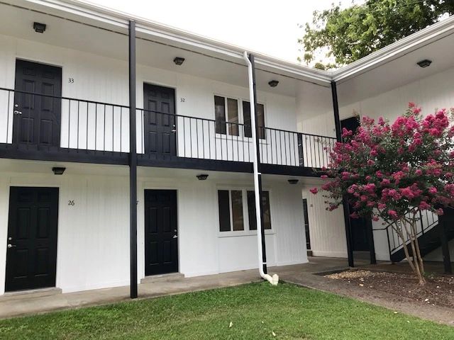 Exterior view of apartment doors with black railings and a blooming pink tree.