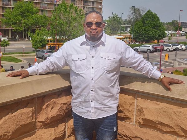 Man in white shirt leaning on a stone railing outdoors.