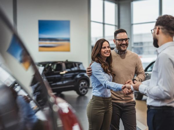 Happy couple shaking hands with a car dealer at a dealership.