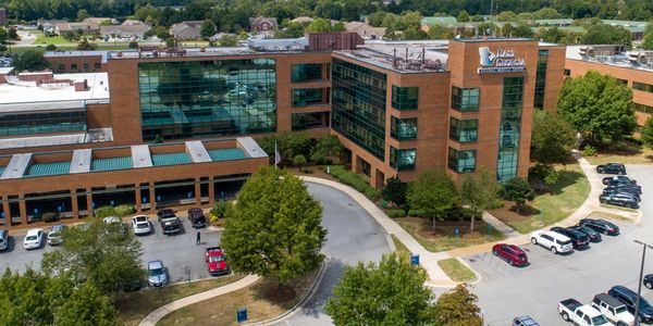 A modern office building surrounded by parking lots and trees.