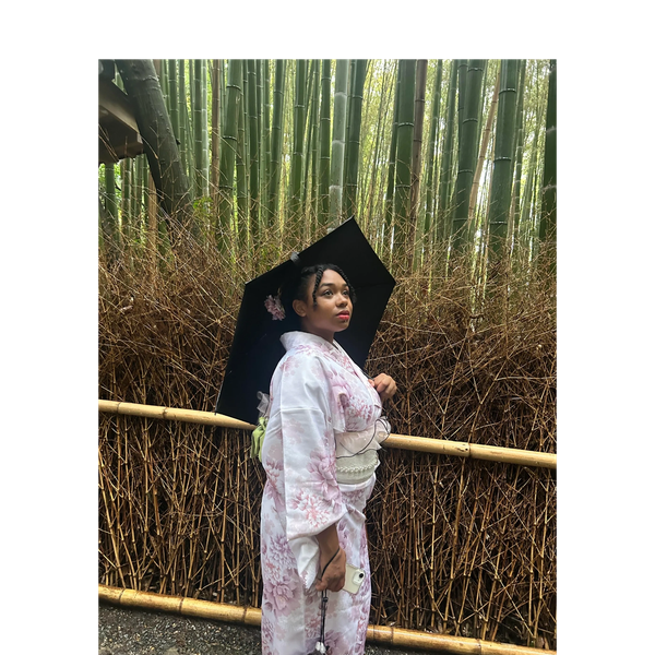 Woman in a white kimono holding a black umbrella in a bamboo forest.