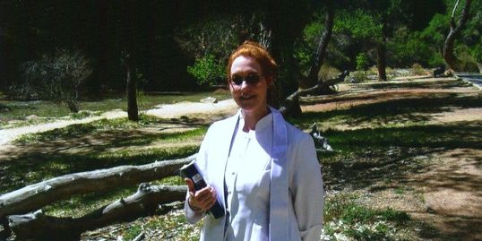 Dr. Red in white cassock, holding Recovery Bible with nature scene in the background