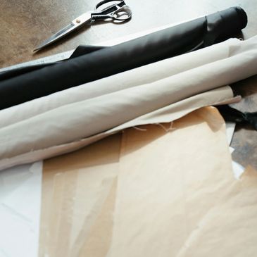 Scissors, fabric rolls, and pattern papers on a wooden table for sewing.