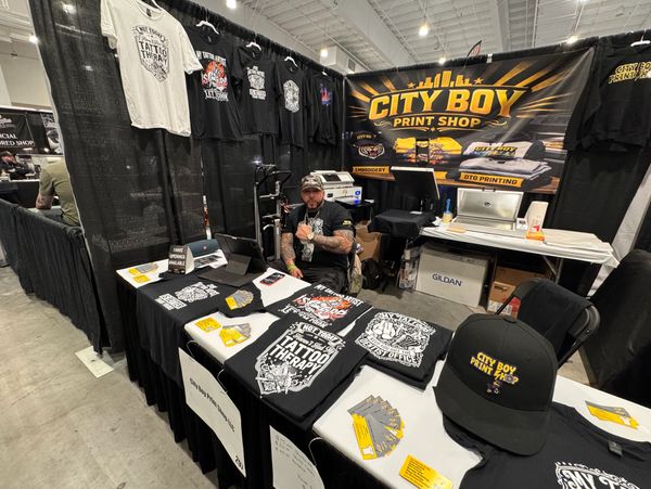 City Boy Print Shop booth with a man showcasing t-shirts and merchandise.