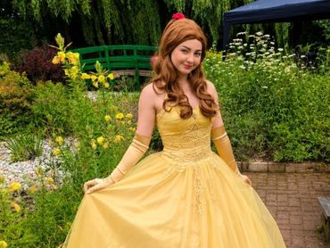 Woman dressed as Belle from Beauty and the Beast in a garden.