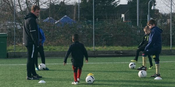 Coach training young kids in soccer on a field with balls and cones.