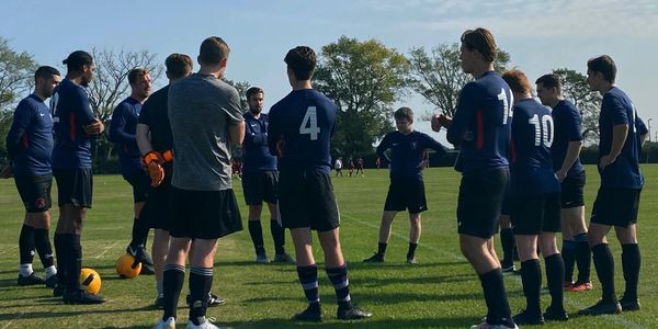 A soccer team gathers in a circle on a sunny field for a discussion.