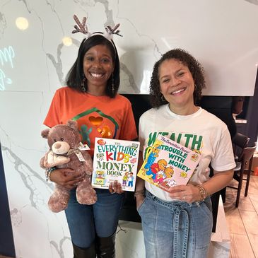 Two women smiling, holding children's books and a teddy bear.