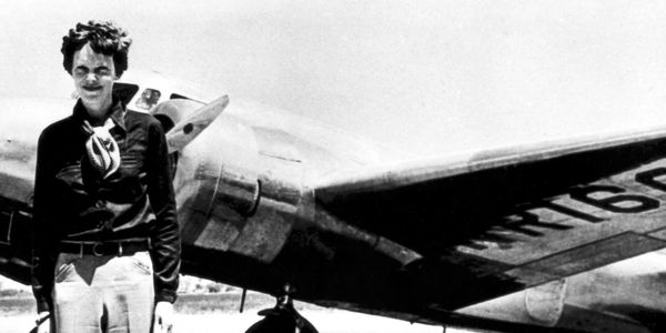 Amelia Earhart standing beside her aircraft, showcasing her pioneering spirit in aviation.