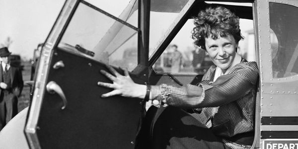 Amelia Earhart sitting in an airplane cockpit, smiling.