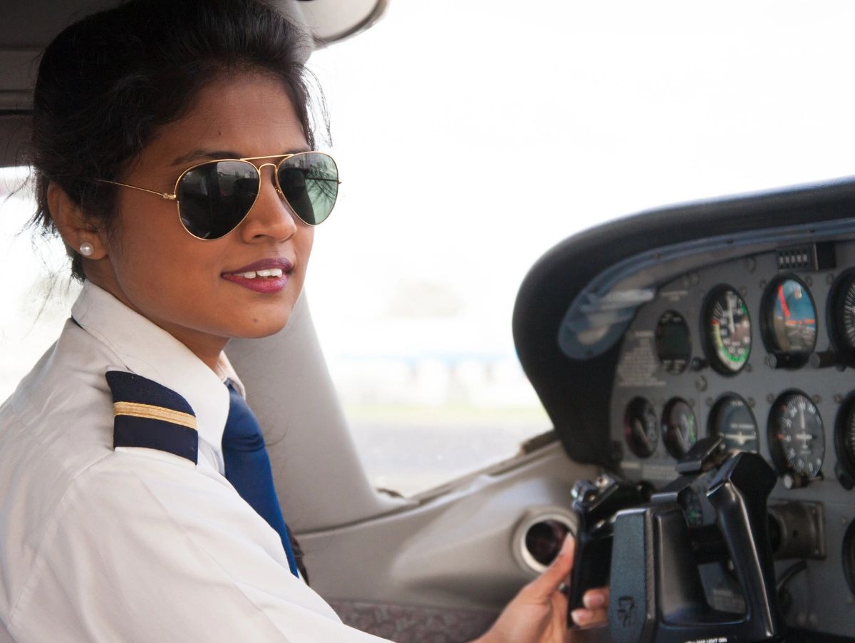 Confident female pilot in uniform with sunglasses inside an airplane cockpit.