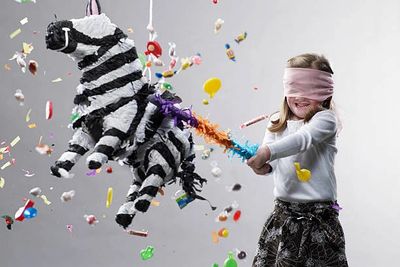 A blindfolded girl breaking a zebra piñata with colorful candies flying out.