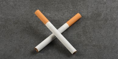 Two cigarettes crossed on a gray surface.