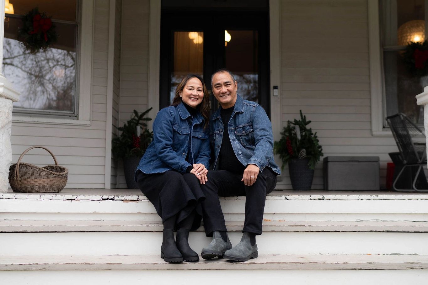 Smiling couple in denim jackets sitting on porch steps.