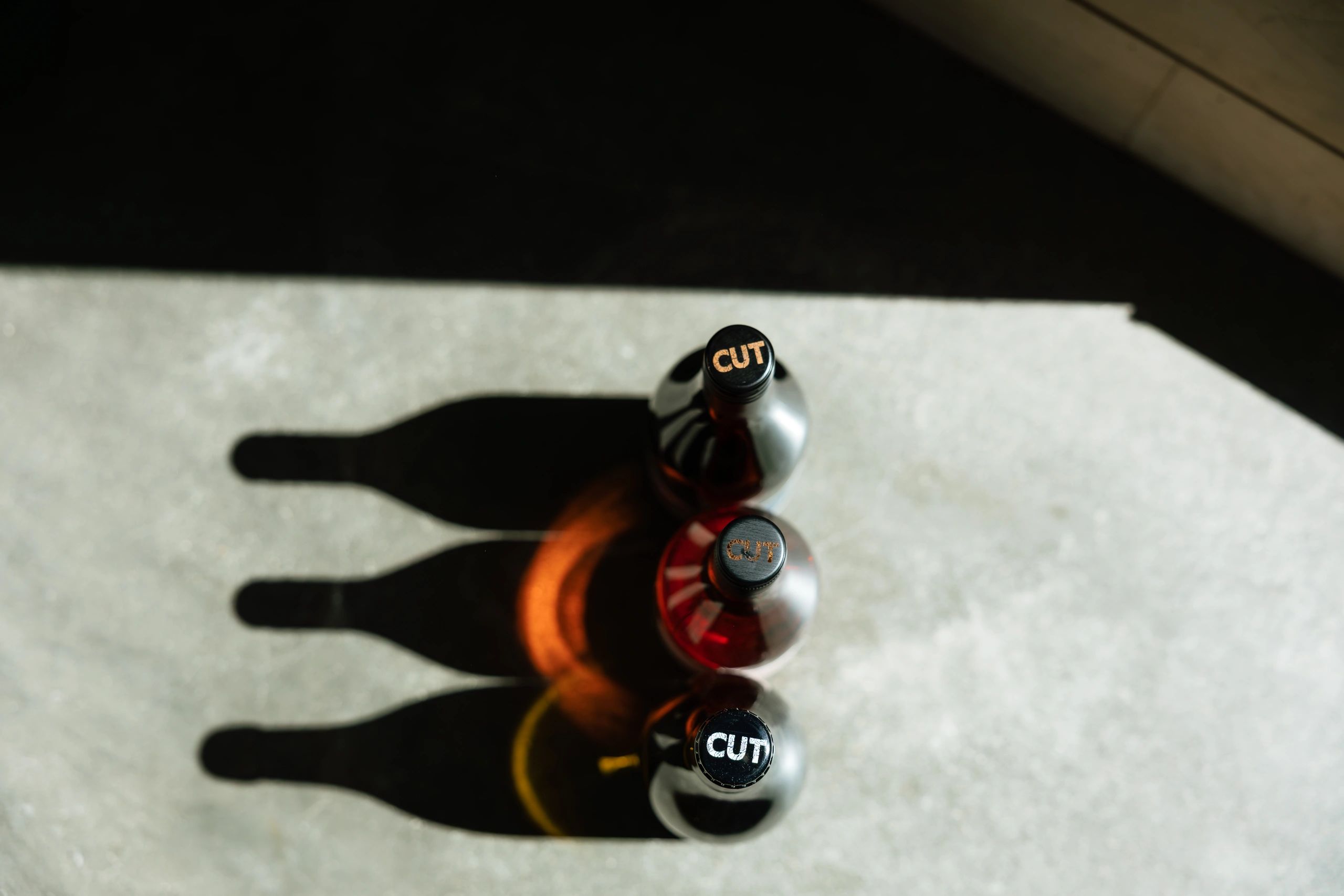 Three bottles with "CUT" caps casting long shadows on a concrete surface.