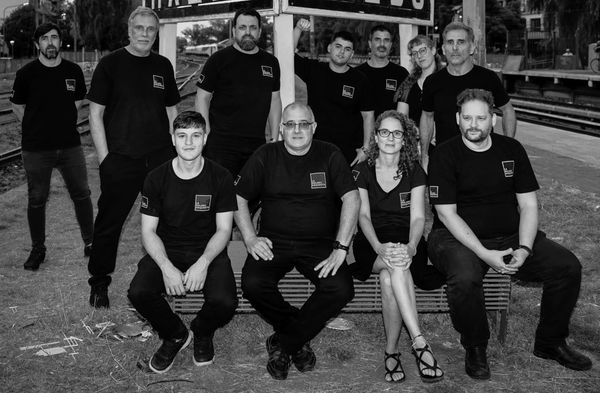 Group portrait of eleven people in matching black shirts at an outdoor location.
