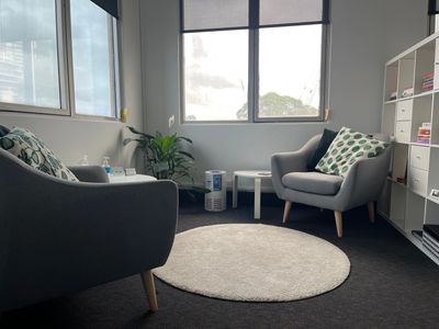 Cozy office corner with two armchairs, a round rug, and natural light from large windows.