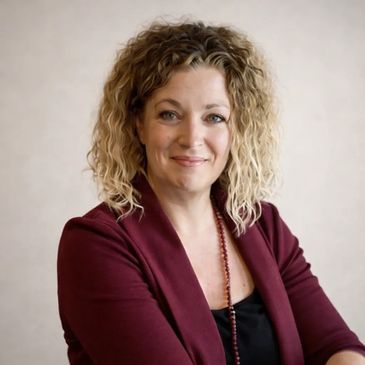 Confident woman with curly hair wearing a burgundy blazer.