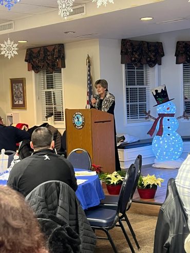 A woman speaks at a podium during a winter-themed indoor event.