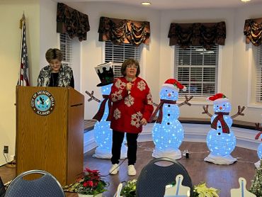 Woman speaking at podium with holiday snowman decorations behind her.