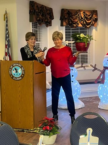 Two women at a City of Hickory Hills event, one holding a microphone, the other a flower pot.