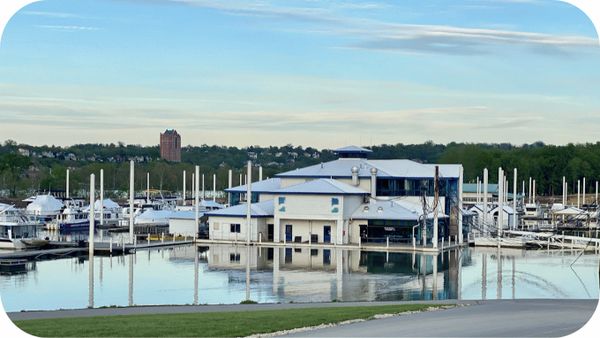 Marina with boats docked around a central building on calm water under a blue sky.