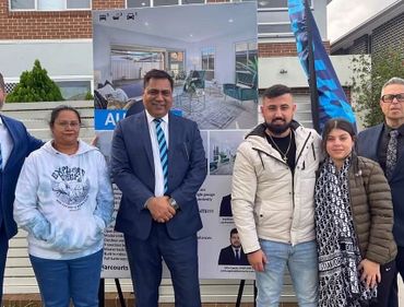 Group of five people posing outdoors near a real estate poster.