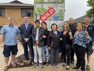 Group celebration in front of a sold house sign.