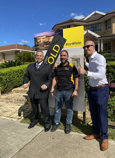 Three men celebrating a home sale with a sold sign in front of a house.