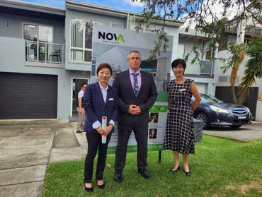 Three real estate agents standing in front of a modern house for sale.