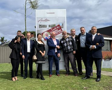 Group of professionals posing outdoors in front of a real estate sign.