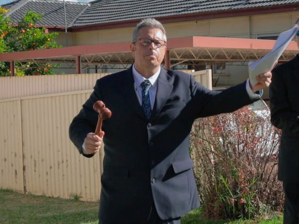 Man in suit holding a gavel and papers outdoors.