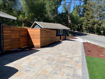 A paved driveway next to a wooden fence and small shed.