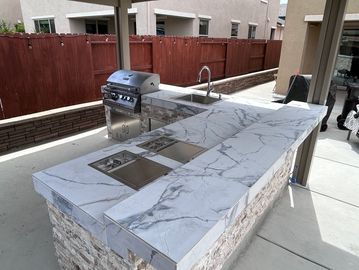 Outdoor kitchen with marble countertop, built-in grill, and sink.