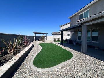 Modern backyard with artificial grass and rock landscaping under a clear blue sky.