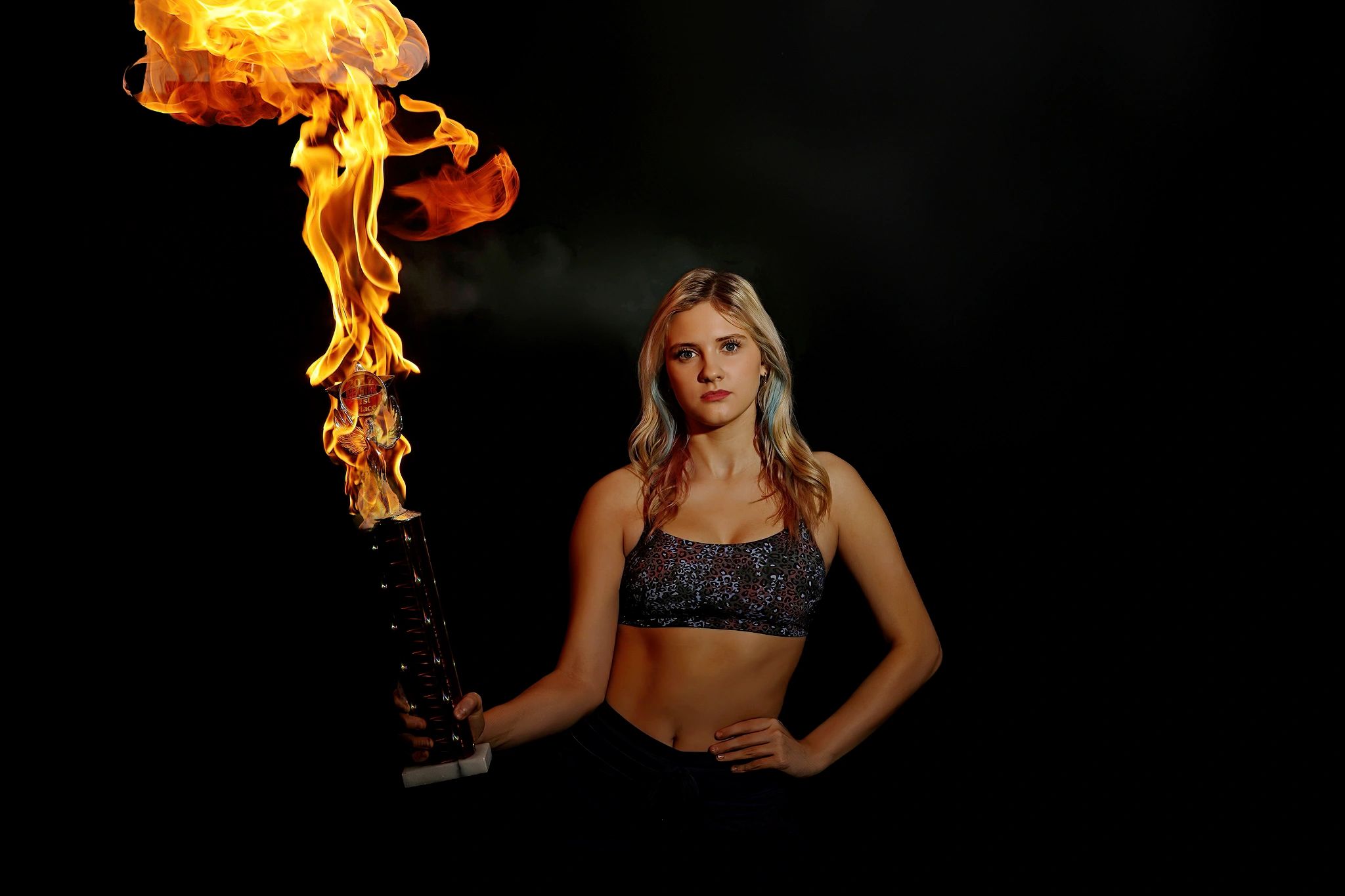 Athletic woman holding a flaming trophy against a dark background.
